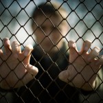 shutterstock_74741107 man in prison hands on fence