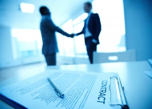 Two people shaking hands with a contract on the table