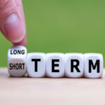 Hand turns a dice and changes the expression "SHORT TERM" to "LONG TERM" (or vice versa).