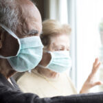 old man and woman with mask looking through window