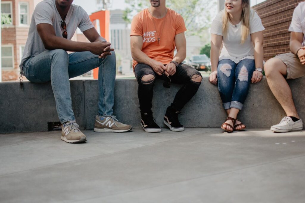 A group of people sit on a low wall, you can't see their faces, but they look like they are talking to each other