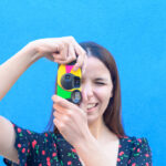 Funny caucasian girl in casual outfit is taking a pictures with a vintage camera outdoor - Summer, joy, relax, concept - close up portrait, coloured background with a space for advertising