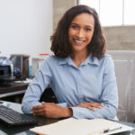 Young,Female,Professional,At,Desk,Smiling,To,Camera