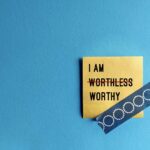 Note stick on copy space blue background with text I AM WORTHLESS change to I AM WORTHY, concept of self talk affirmation to overcome low self esteem, to love and accept value of oneself