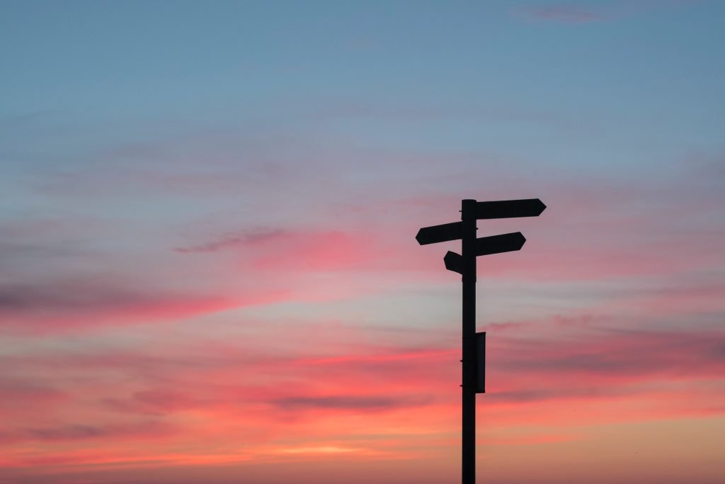 a bright pink sunset, with the silhouette of a sign (pointing in multiple directions) in front