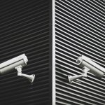 two cctv cameras point in opposite directions on the corner of a building, a black and white picture
