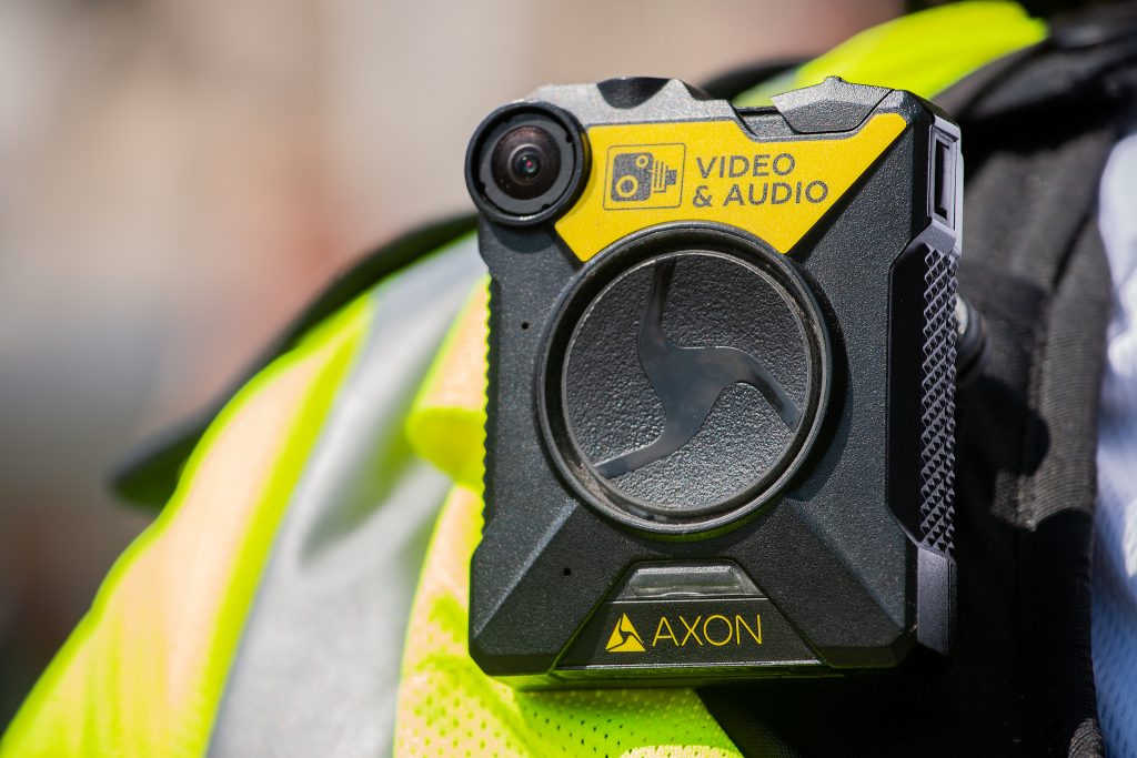 A yellow body worn camera on the shoulder of an official wearing a yellow high visibility vest