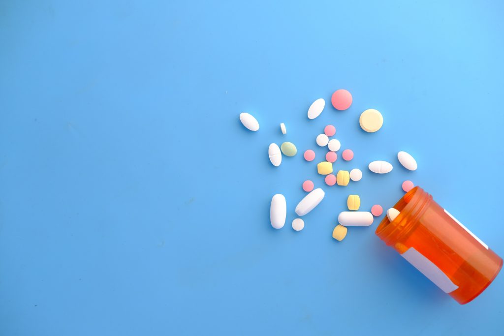 An orange pill box has tipped over onto a blue background, with many tablets of different sizes and colours spilling out