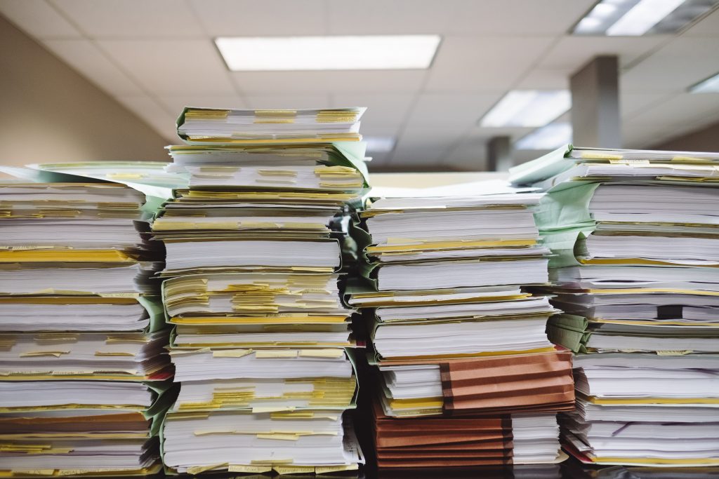 Several stacks of papers and files are piled up on top of each other in an office