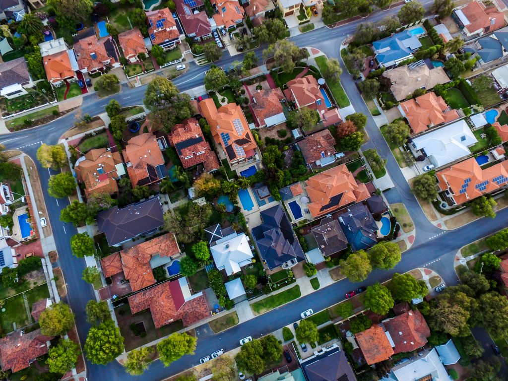 Many houses are seen from above, some have terracotta roof tiles, others have swimming pools in their back gardens