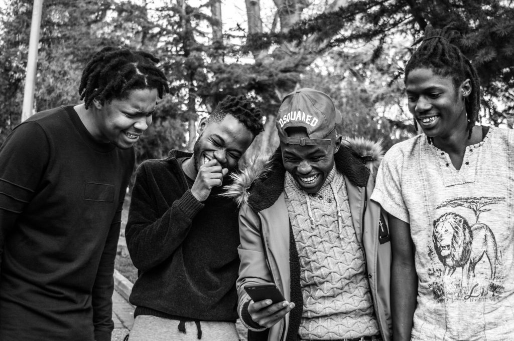 A group of young black men are gathered around a phone and they are laughing