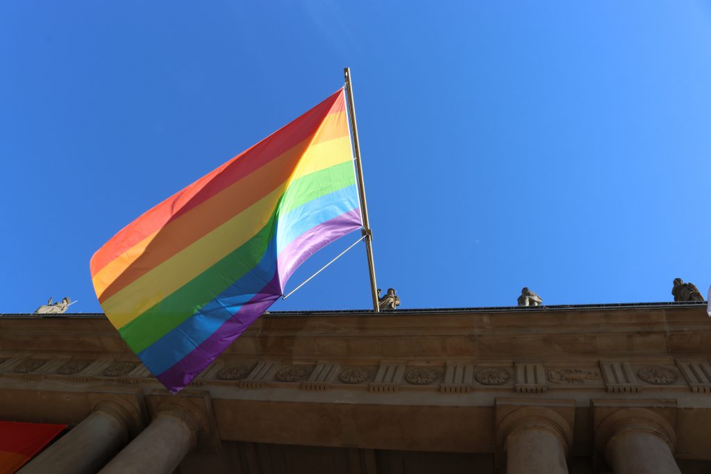 LGBTQi+ poster hangs from a building in front of a blue sky