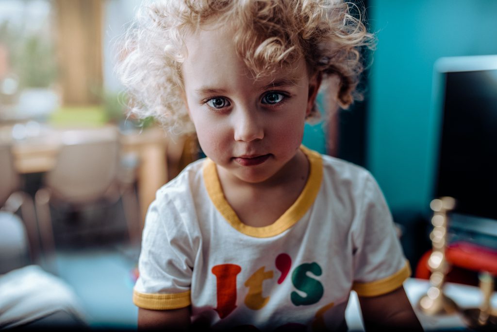 a young child with curly blonde hair and light eyes looks into the camera
