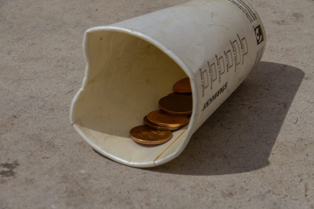 A tipped over starbucks cup on the floor has a few pennies inside. 