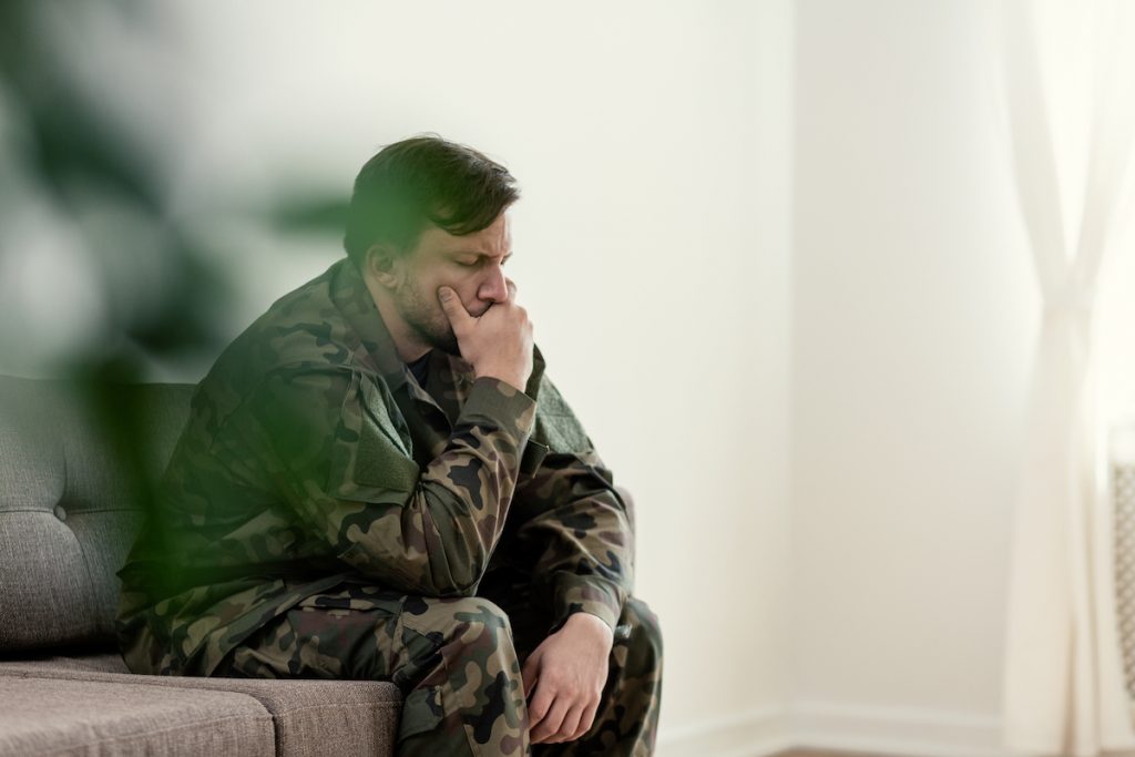 Sad soldier in uniform covering his mouth while sitting on a sofa