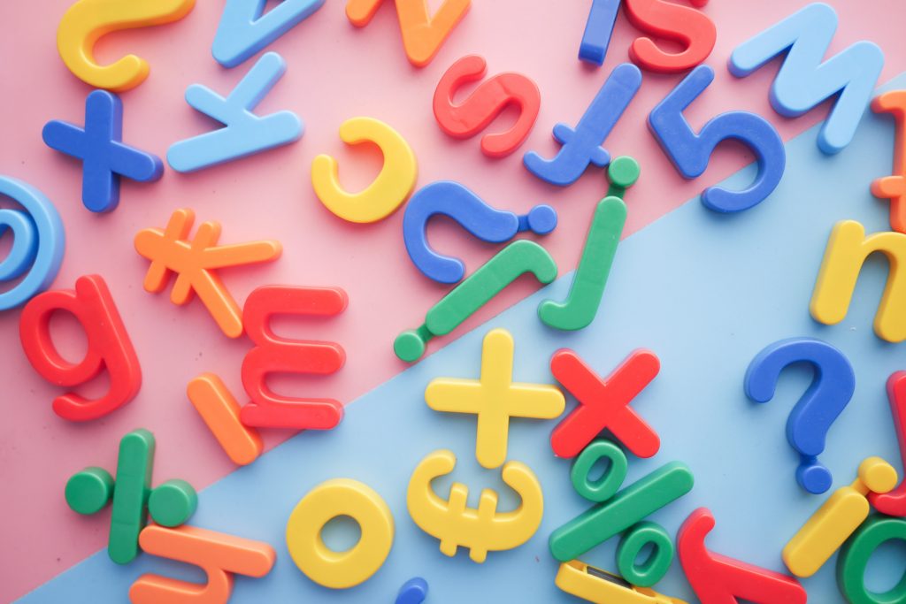 multicoloured letters and symbols lie flat on a light pink and blue background. 