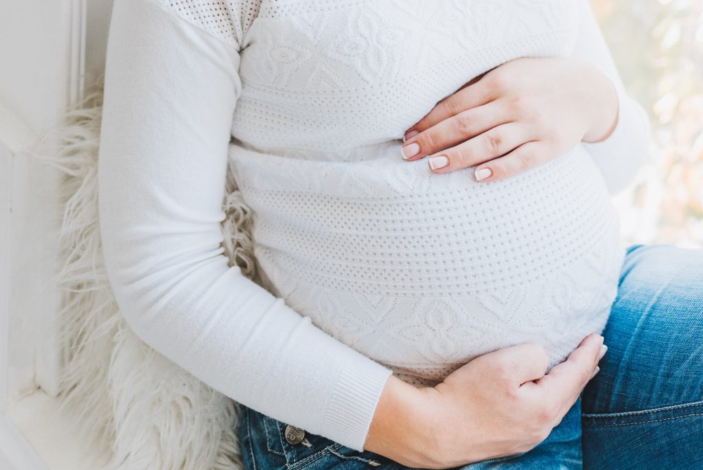 a pregnant woman in a white top cradles her baby bump