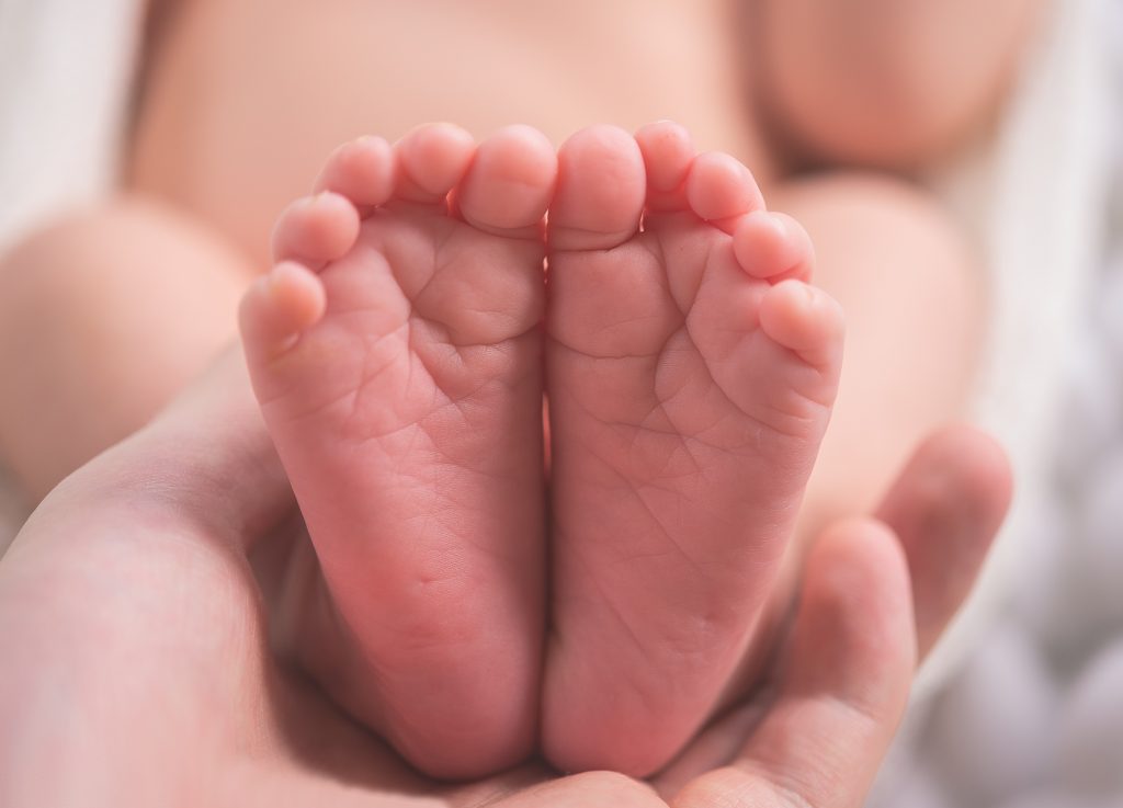 pink baby feet face the camera, and they are being held underneath by an adults hands