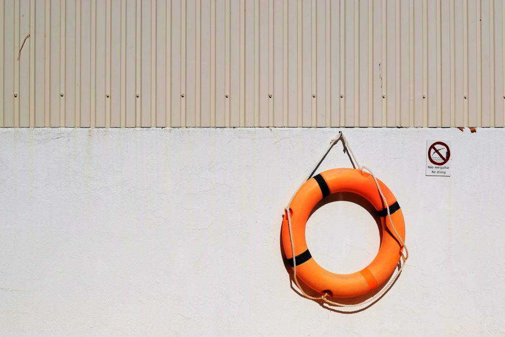 an orange round life buoy hangs on a white wall