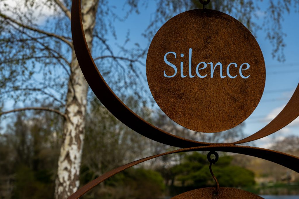 a brass coloured sculpture in a garden says the word 'silence'
