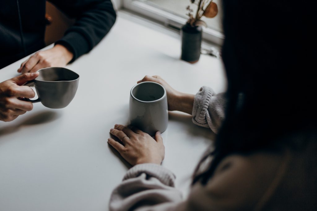 two people sat across a white table by a window, with white coffee cups in hand