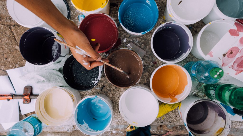 pots of different coloured paint are open and a hand with a paint brush is dipping into a brown paint point