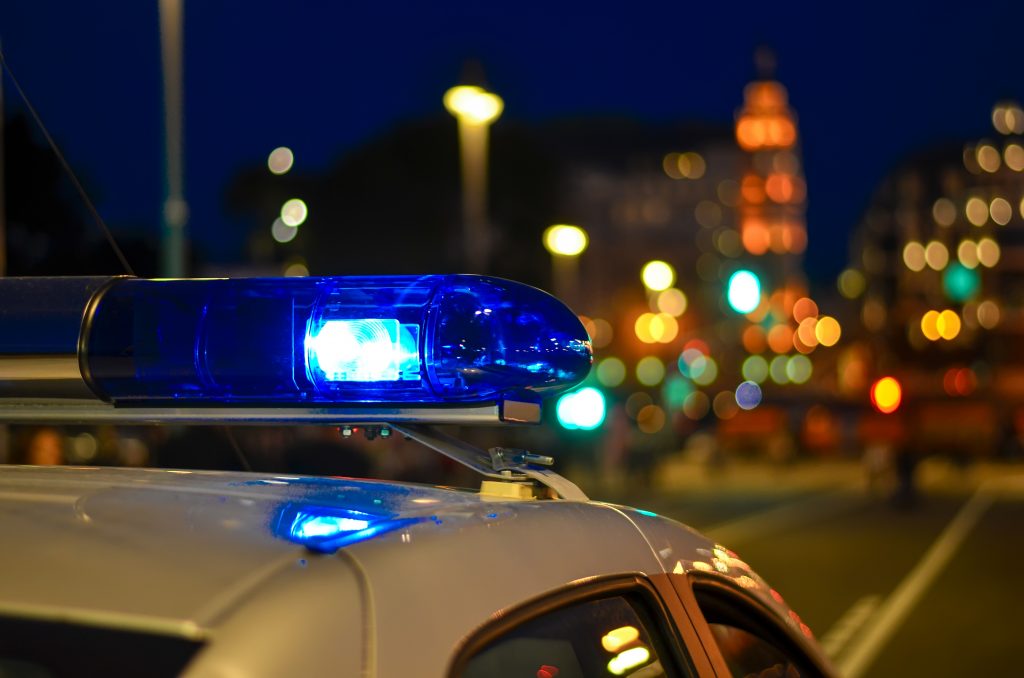 The blue light of a police car shines in front of blurred city lights.