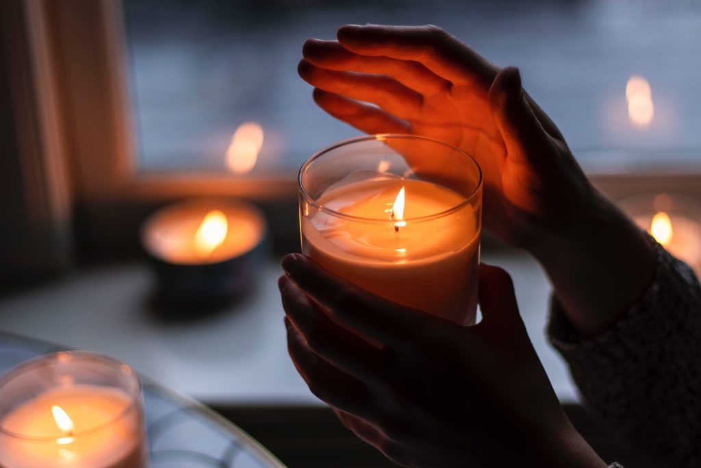 a pair of hands are holding a candle and are lit by the candlelight