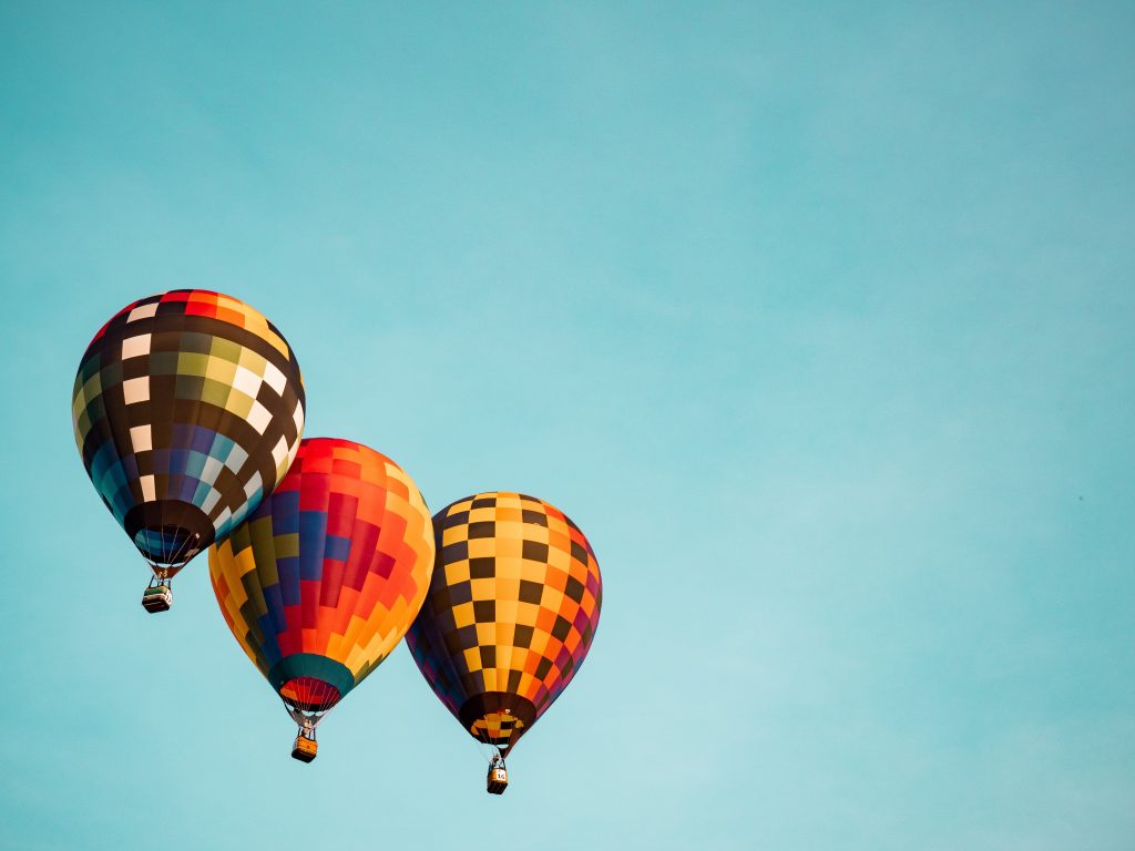 three hot air multi coloured hot air balloons fly against a blue sky