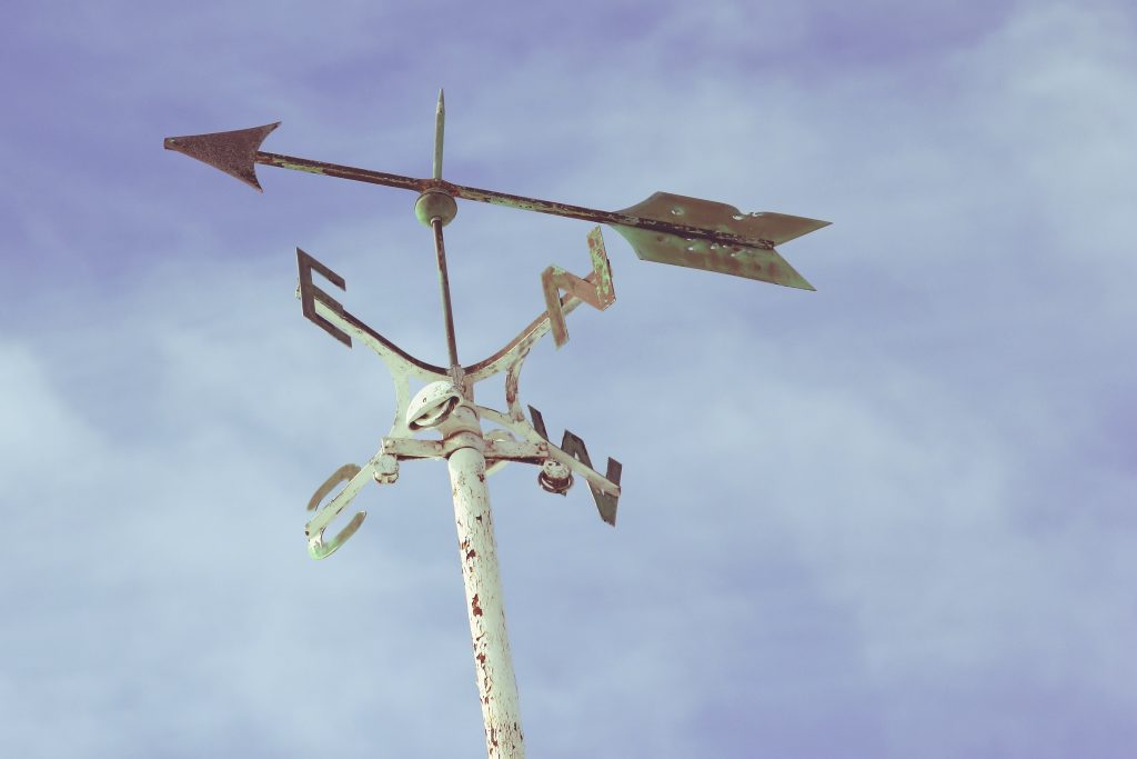 a white metal arrow points south east, aboe metal spokes pointing North, South, East and West.