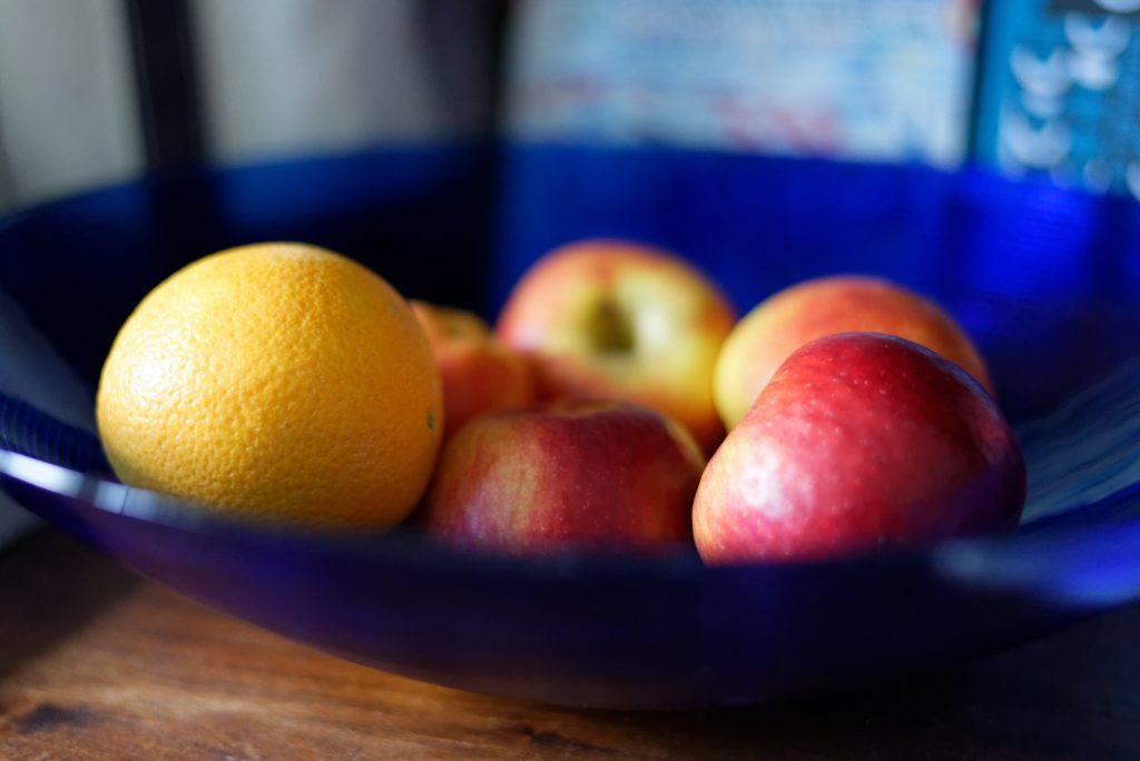 apples and oranges sit in a blue bowl