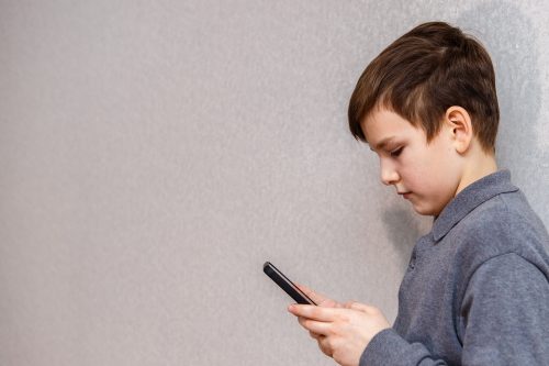 Boy,Ten,Years,Old,Standing,And,Looking,At,Smartphone.,Portrait