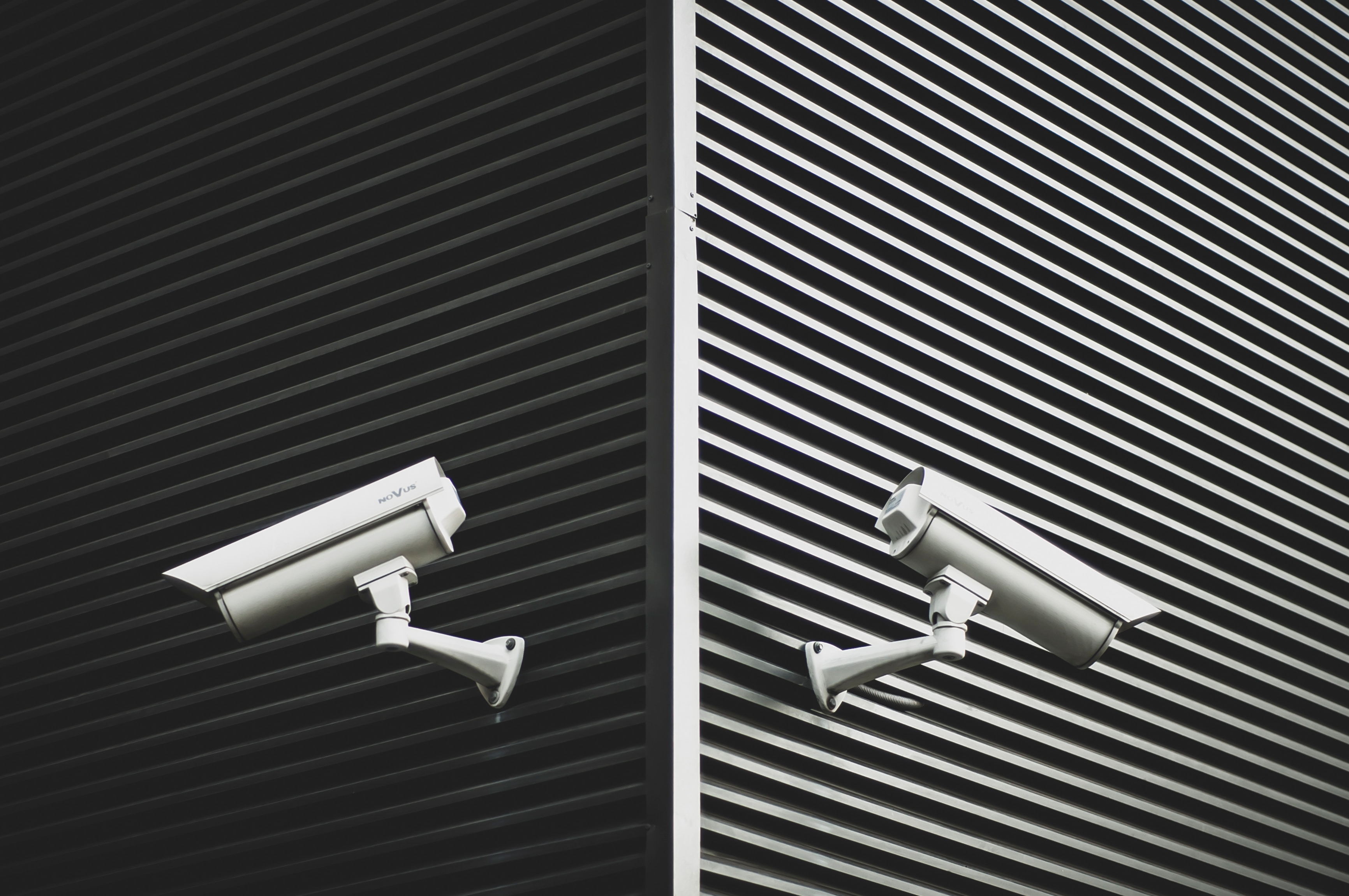 two cctv cameras point in opposite directions on the corner of a building, a black and white picture