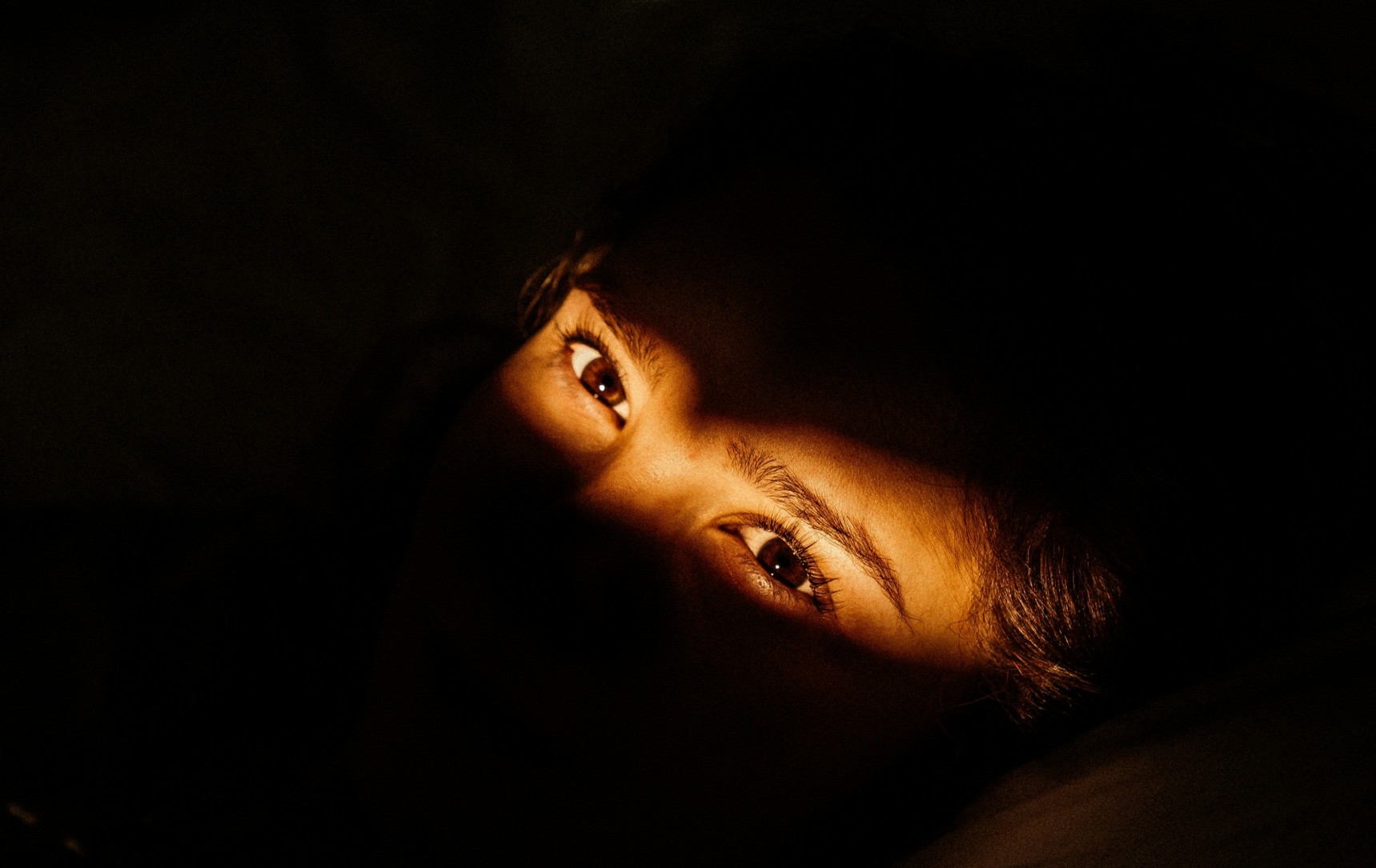 A pair of open eyes lit but surrounded by darkness.