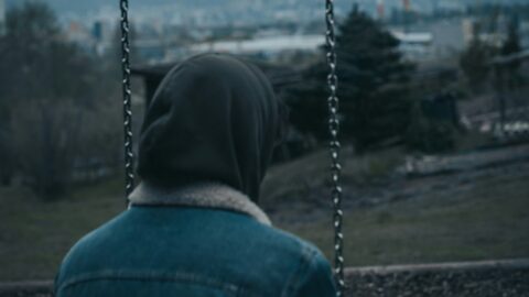 Short from behind of person sitting on swing with hood up