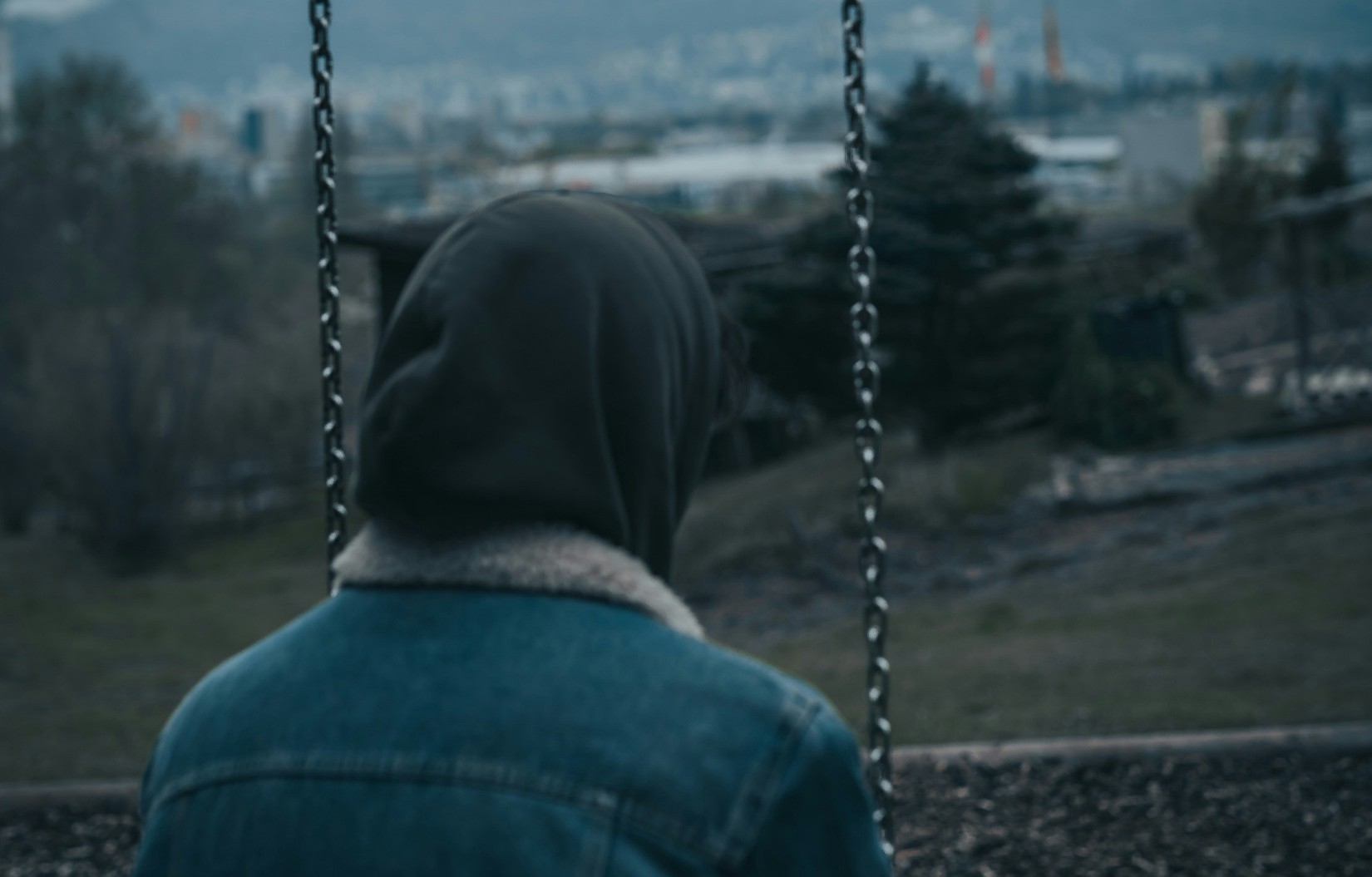 Short from behind of person sitting on swing with hood up