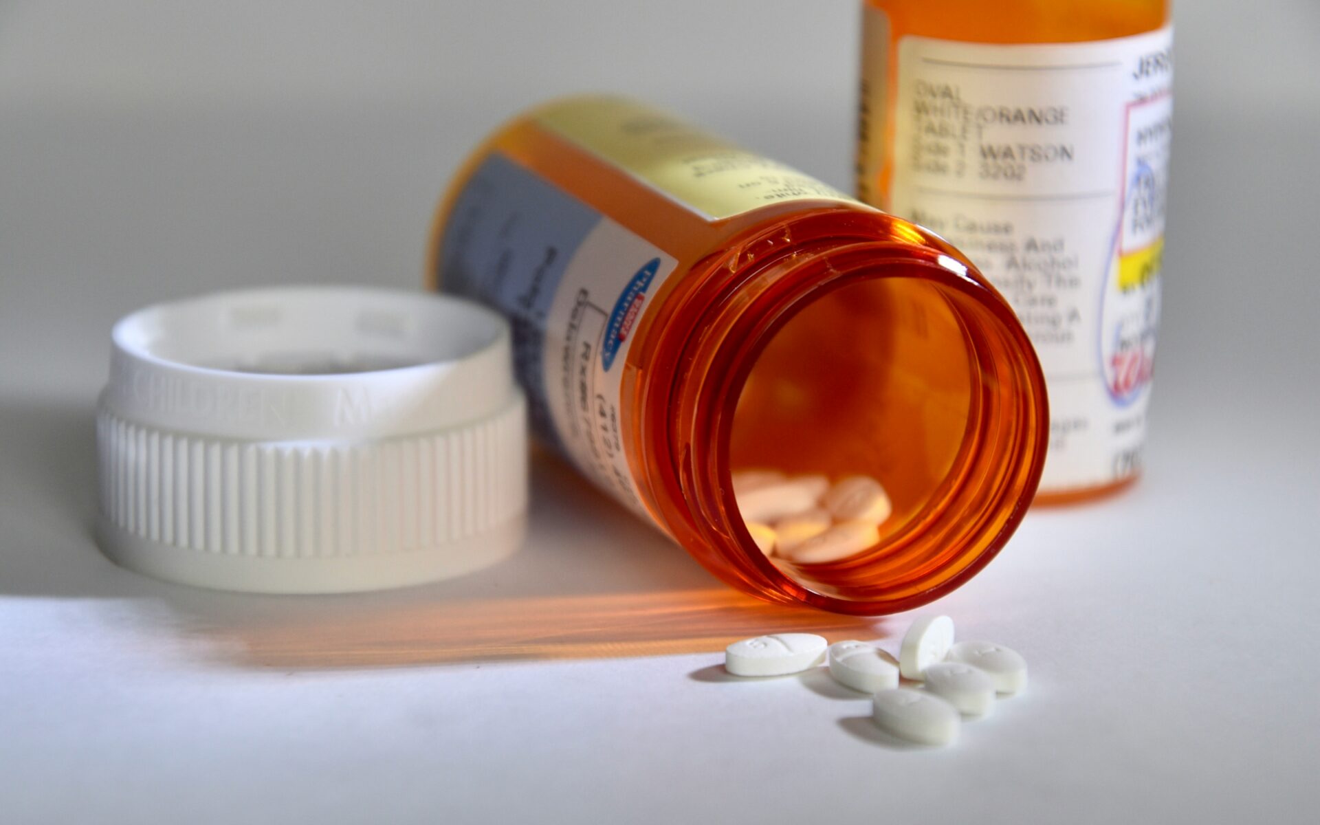 A pill container lies on its side with white pills spilling out