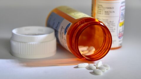 A pill container lies on its side with white pills spilling out
