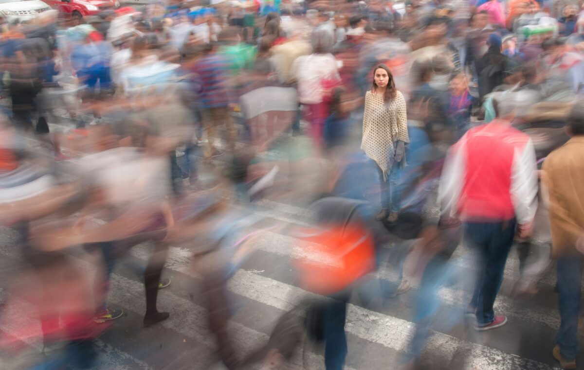 Woman stands still amongst a fast moving, blurred crowd