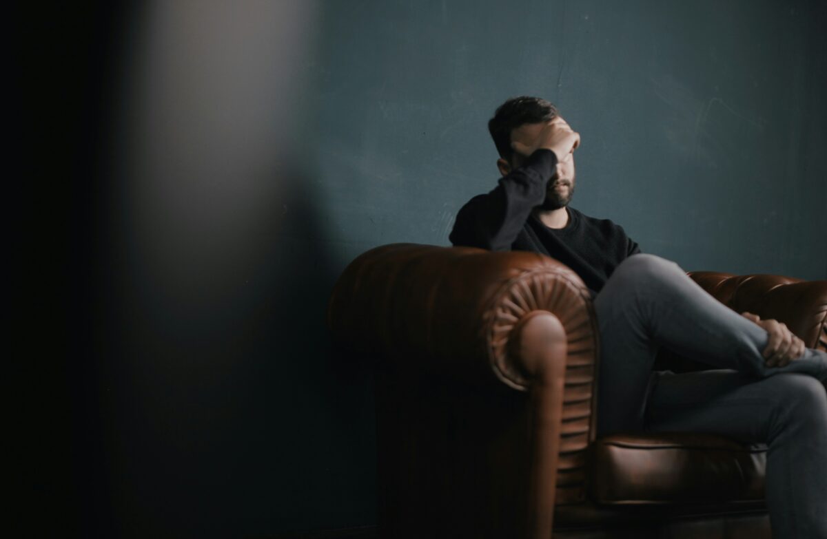 a-man-holds-his-head-while-sitting-on-a-sofa