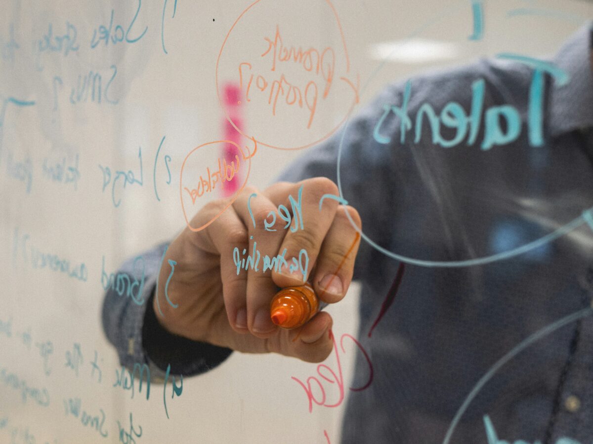 Person writing on clear board with coloured marker
