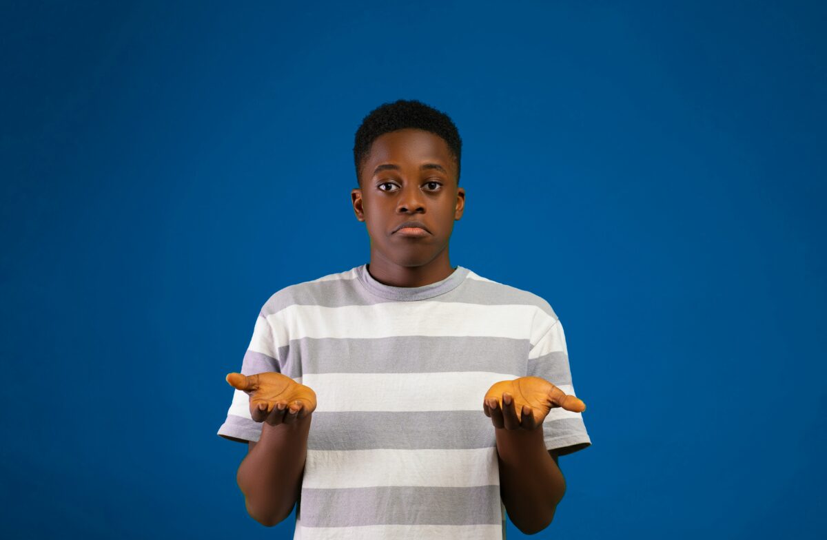 A boy holds up his hands, palms facing up, with questioning facial expression.