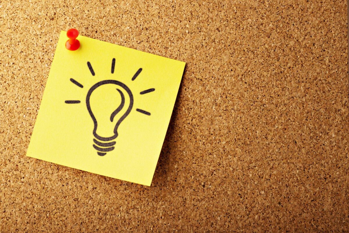 A yellow sticky note with a lightbulb drawn on it is pinned to a cork notice board