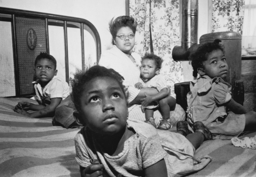 Black and white photo of Windrush Generation family all sitting on big double bed
