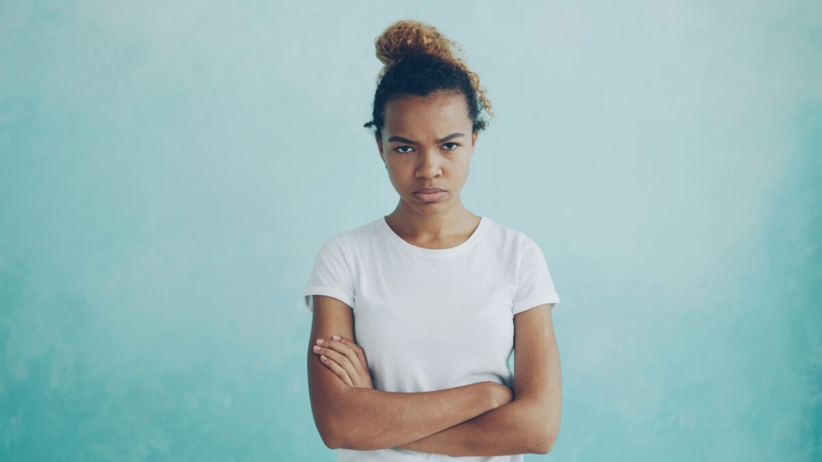 A teenage girl frowning at the camera with her arms crossed